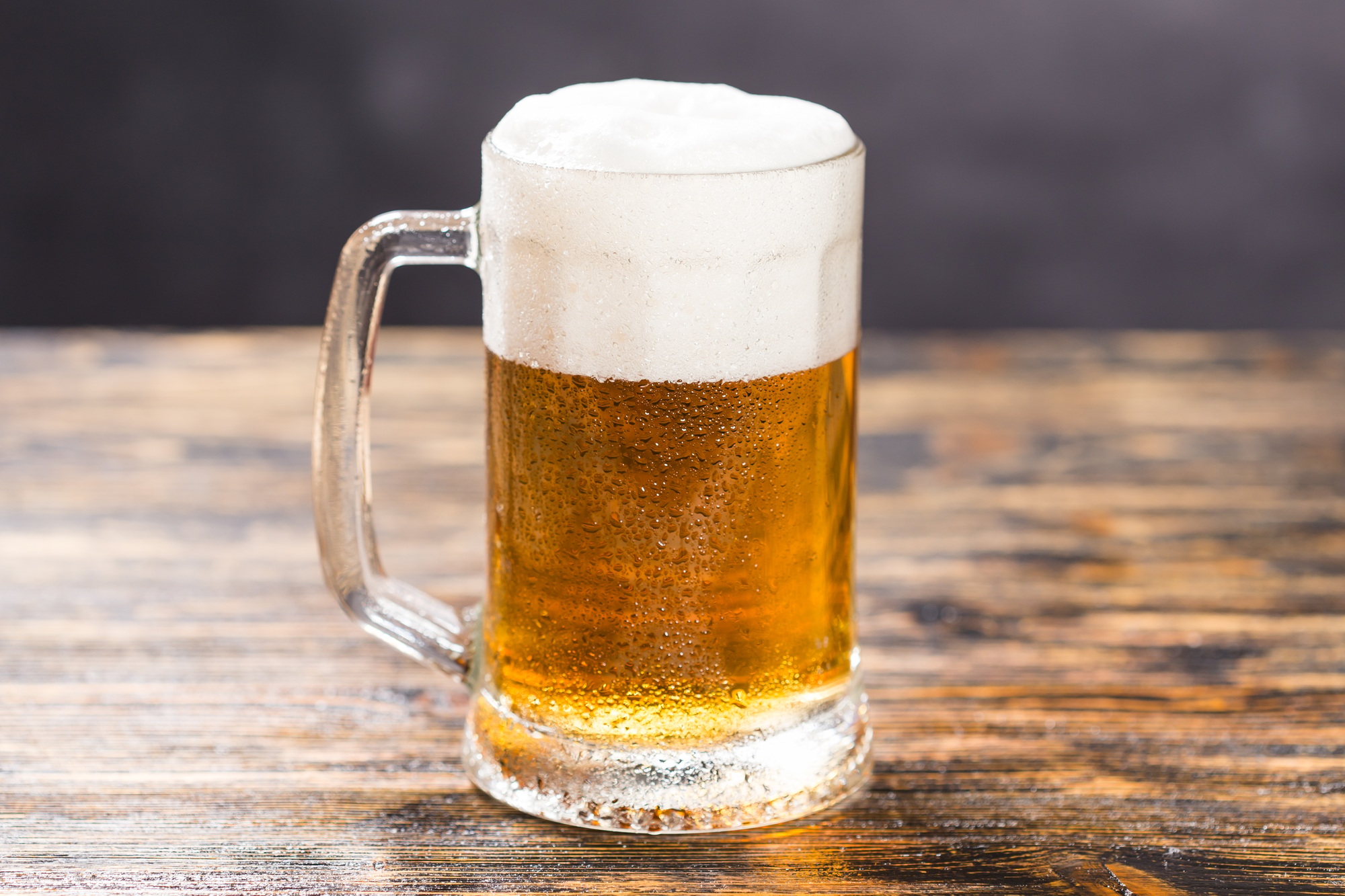 Mug of cold pale beer placed on a rustic wooden table with copy space
